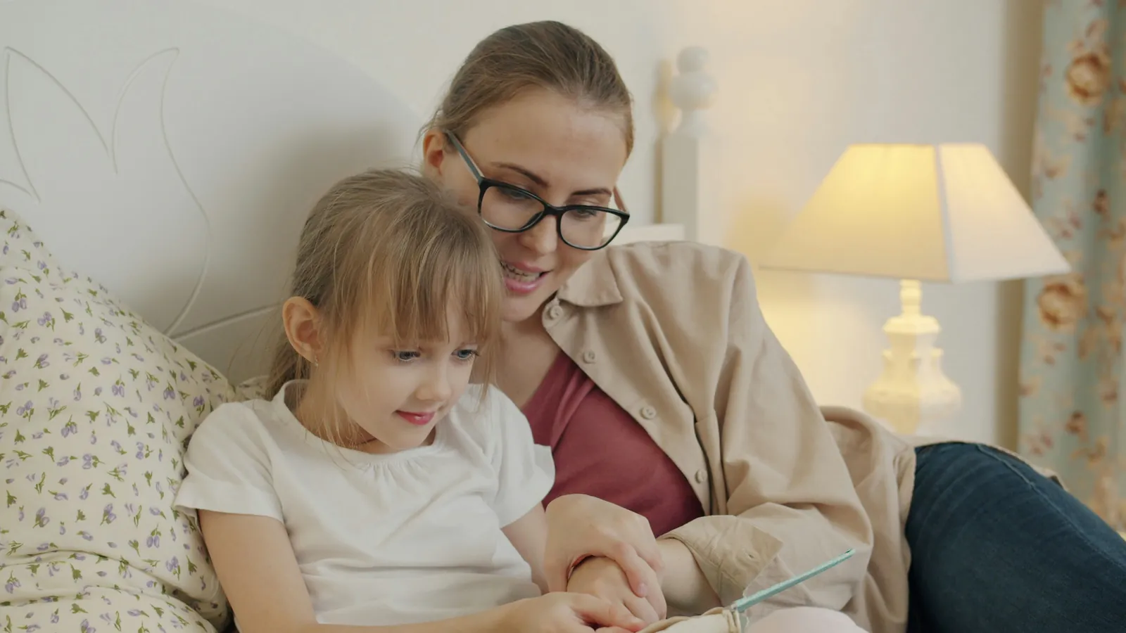 A mum reading a book with her young daughter at home in warm lamplight